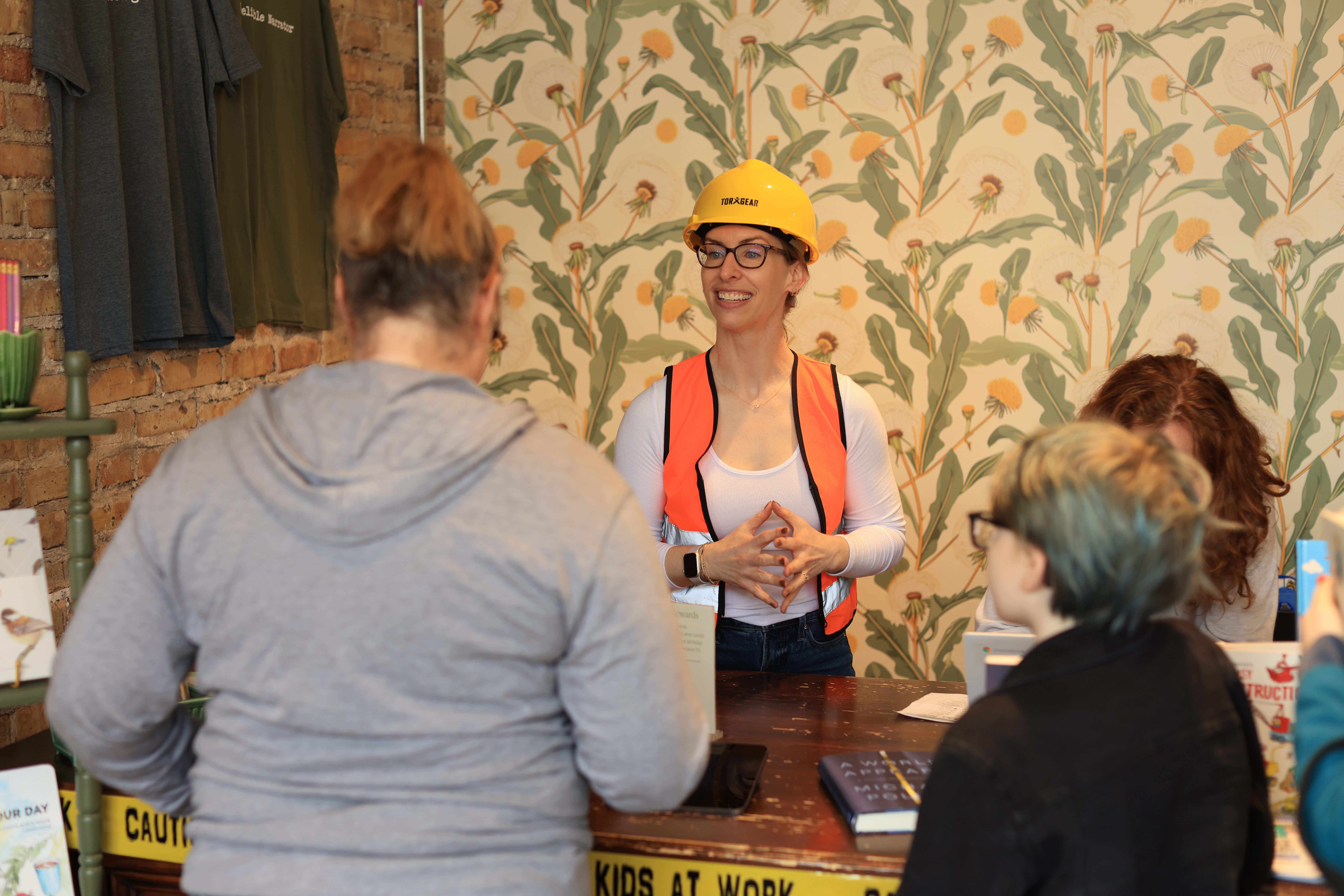 Jamie Ericson, owner of Dandelion Bookshop, speaks with customers while wearing a yellow hat